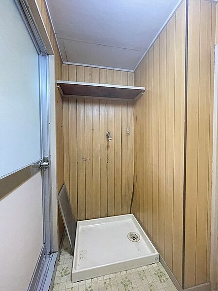 木目調の壁が特徴的な洗面所です。シンプルな棚が設置されており、上部には収納スペースも確保されています。
