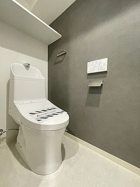 落ち着いたアクセントクロスが印象的なトイレ空間。収納棚も備え付けられており、すっきりと清潔感を保てます。日々の快適を支える設備です。