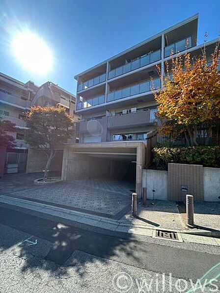 陽光あふれるエントランス。明るい日差しが、建物の洗練された外観と植栽を優しく照らします。