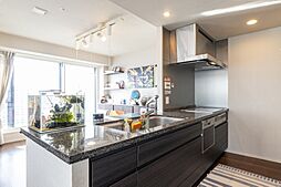 【天然石の煌めき】開放的なフルフラットキッチンが主役。上質な御影石の天板や充実の設備が、日々の料理を特別な時間に。リビングの大きな窓から光が溢れ、洗面室まで統一された美学が宿る、都心の洗練された邸宅。