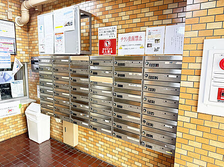 綺麗に清掃されたダイヤル式の集合ポスト。掲示板やゴミ箱も整然と配置され、管理が行き届いています。