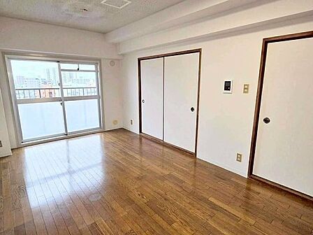 光沢のある木目調フローリングと白壁のコントラストが美しい室内です。バルコニーへ繋がる大きな窓から自然光を取り込みやすい構造になっています。引き戸の枠やドア枠の木目が空間の程よいアクセントです。