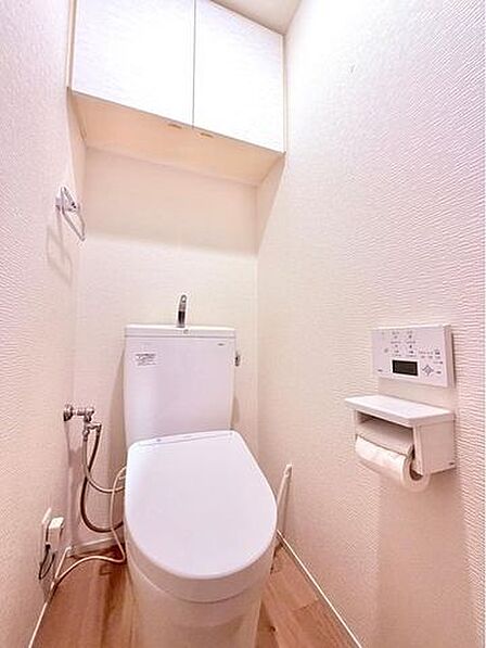 ウォシュレットのついた温水洗浄便座のトイレです。扉付きの吊戸棚もあり、掃除用具や予備のトイレットペーパーなども隠してたっぷり収納できます。壁面のニッチには芳香剤を置いたり、便利にお使いいただけます。