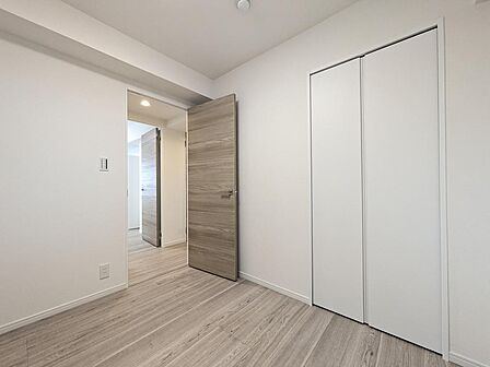 木目調のドアと白いクロスが上品に調和する洋室。コンパクトながらクローゼット完備で、限られたスペースを有効活用できます。扉を開ければ廊下からリビングまで見渡せる、開放的で風通しの良い間取りです。
