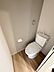 トイレ：シンプルで清潔感のあるトイレです。ナチュラルなフローリングが空間全体に落ち着いた印象を与えます。壁面にタオルリングとペーパーホルダーが設置されています。手入れのしやすい設計です。