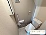 トイレ：シックなアクセントクロスがおしゃれな落ち着きあるトイレ空間です。手洗い付きタンクや手すり、壁面収納を備え、限られたスペースを有効活用した設計になっています。