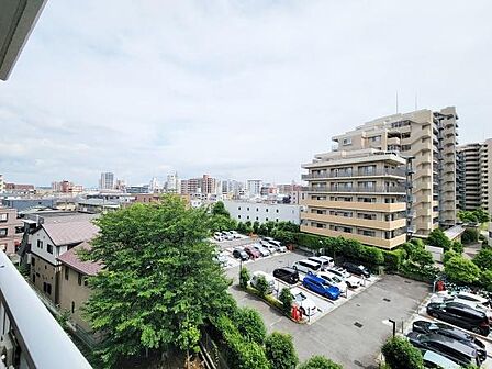 バルコニーから広がる眺望が開放感を演出します。周囲には高層の建物が並び都市らしい景色が楽しめます。駐車場や緑も視界に入り安心感があります。明るい空が全体を包み込む印象です。