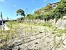 外観：現地土地写真では陽当たりの良い空間が広がっています。道路や周辺の建物との距離感もわかりやすく開放感を感じられます。敷地内は雑草が生い茂っていますが土地の広さや形状が把握しやすい状態です。