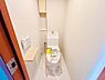 トイレ：清潔感のある明るいトイレです。壁リモコンや収納スペースが設けられており使いやすさに配慮されています。床の色合いが空間をすっきりと見せます。ドアや木目調の棚がアクセントとなっています。