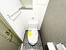 トイレ：シンプルなデザインで清潔感を感じるトイレです。ペーパーホルダーや棚が設置され使い勝手も良好です。壁面のクロスと床材が調和した空間となっています。収納スペースも備えられており機能面も配慮されています。
