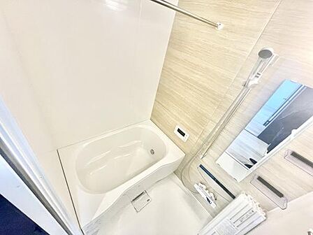 清潔感のあるバス空間です。壁面のデザインが明るく全体的に開放感があります。浴槽とシャワーのスペースがしっかり確保されています。ミラーや収納棚も配置されており使い勝手が考えられた設計です。