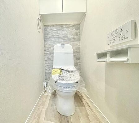 白を基調とした清潔感のあるトイレ空間です。床と壁の組み合わせがシンプルで明るい印象を与えます。背面のアクセントクロスによりデザイン性も感じられます。