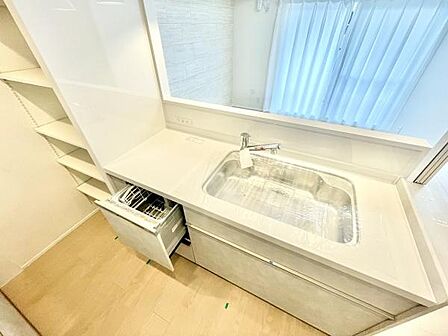 カウンター付きのシンクが明るい印象です。収納棚があり使い勝手の良い空間です。食洗機も設置されており利便性が感じられます。キッチン周りがすっきりとまとまっています。