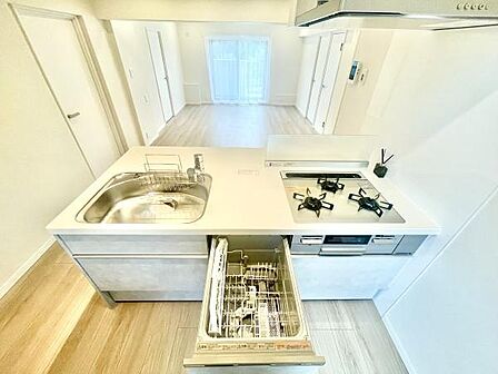 キッチンはシンプルで明るい印象です。ガスコンロや食器洗い乾燥機が設置されています。作業スペースが広く料理の準備も快適に行えます。シンクも大きめで使い勝手が良いです。室内がすっきりとまとまった印象です。