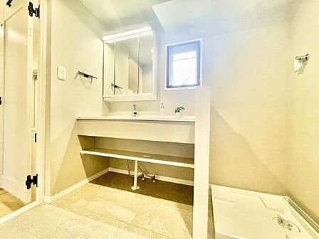 明るい空間が広がる洗面台・洗面所です。大きなミラーと収納棚が設置されており使い勝手の良さが感じられます。窓からの自然光が入り清潔感のある印象です。動線が確保されていて利便性にも配慮されています。