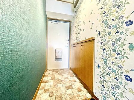 玄関は明るく清潔感のある空間です。フローリングとクロスのコントラストが特徴的です。壁面には自然を感じさせるデザインが施されています。収納スペースもしっかり確保されています。