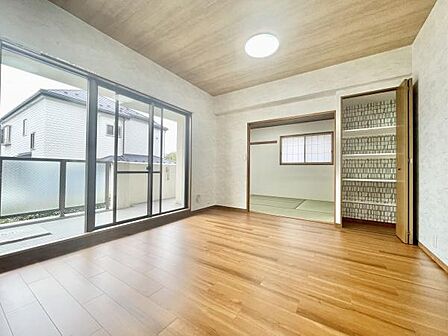 大きな窓からたっぷりと自然光が差し込みます。リビングには和室も隣接しており空間の広がりを感じられます。木目調の床と天井が落ち着いた雰囲気を演出しています。収納スペースも確保されています。