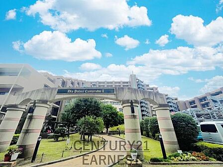 印象的なアーチ型のエントランスが特徴の外観です。緑豊かな植栽がエントランス周辺を彩っています。青空が広がる中建物全体が開放感のあるデザインです。大きく見やすい建物名表示もポイントです。