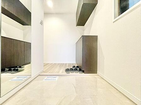 玄関には大きな姿見が設置されており毎日の身だしなみチェックに便利です。収納スペースが豊富で玄関がすっきりと片付きやすい造りです。明るい印象の床材と壁が開放感を演出しています。