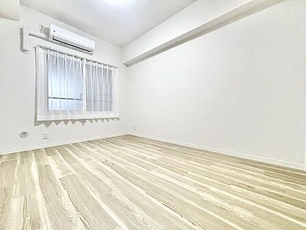 明るい色合いの床が特徴的な寝室です。窓から自然光が差し込み開放感があります。エアコンが設置されており快適な空間を保つことができます。シンプルで使いやすいレイアウトです。