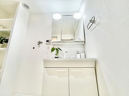 明るい照明が洗面台全体をしっかり照らします。収納スペースも豊富で整理しやすい設計です。白を基調とした空間が清潔感を演出しています。壁面には便利なタオル掛けも設置されています。