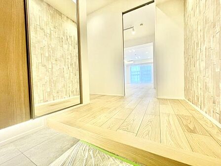 玄関は広々とした空間が確保されており明るい印象を与えます。木目調の床材がやさしい雰囲気を演出しています。大型のミラーが設置されており空間を広く見せています。