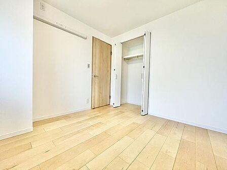 明るい色合いのフローリングが特徴の洋室です。シンプルな内装で家具の配置もしやすい空間です。クローゼットがあり収納スペースも確保されています。木目調のドアがアクセントになっています。