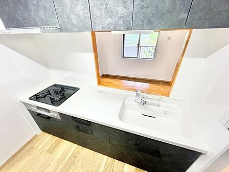 キッチンはシンプルなデザインで白と黒のコントラストが印象的です。カウンターに広がりがあり開放感を感じられます。ガスコンロとシンクがバランスよく配置されています。収納スペースも確保されています。