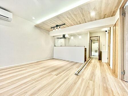 明るい色合いのフローリングがリビング全体を開放的な印象にしています。天井の木目調デザインが空間にアクセントを加えています。ライティングレールが設置されており照明演出も楽しめます。