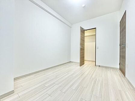 シンプルで落ち着いた色味の床が印象的です。無駄のない壁面が空間を広く見せます。扉付きの収納スペースが備わっています。すっきりとした内装でまとまっています。清潔感がある寝室です。
