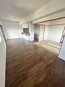 リビングは広々とした空間設計で床材の質感が特徴的です。和室が隣接しており空間に変化をもたらします。窓からの採光が室内を明るくしています。壁の色合いが落ち着いた雰囲気を演出しています。