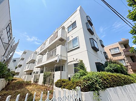白い外壁の集合住宅と植栽のある前面道路