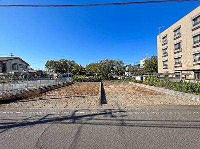 外観：建築前の区画された更地周辺に住宅や建物が見える