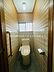 トイレ：木目調の壁とタイルが調和した落ち着いた雰囲気のトイレ空間です。窓付きで自然光が入るため明るさを感じられます。手すりが設置されており使いやすさにも配慮されています。清潔感のある内装もポイントです。
