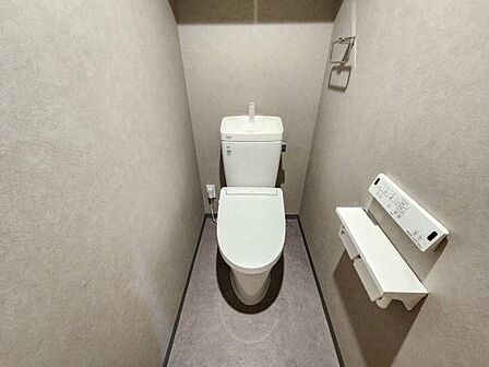 グレーを基調としたトイレです。上部収納棚を備えた新品の温水洗浄便座つきです。