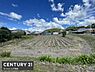 外観：広々とした現地土地写真です。周辺には家屋や緑が広がり開放感のある雰囲気が特徴的です。空や景観も良好な印象を受けます。道路へのアクセスもしやすい立地です。見通しの良い土地が魅力です。