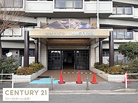 建物のエントランスは広々としています。屋根付きのアプローチが重厚な印象です。緑の植栽が正面を彩り整然とした外観が際立ちます。安心感のある門構えが特徴的です。マンションの名前がしっかり表示されています。