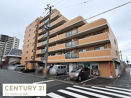 ブラウン系の外観が印象的なマンションです。道路に面していて利便性を感じます。角部屋やバルコニーが多く配置されています。1階にはテナントも入っています。駐車スペースも確認できます。