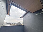 バルコニーから広がる空の景色が印象的です。屋根付きで天候に影響されにくい設計となっています。壁面のシンプルなデザインが空間に落ち着きを与えています。周囲の住宅地が見渡せる開放感も魅力です。