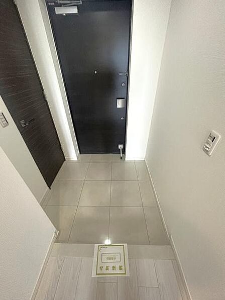 明るいホワイト系の壁面と高級感のある床タイル、シックな扉が美しく調和した玄関ホールです。落ち着いた質感のタイル敷きとなっております。
